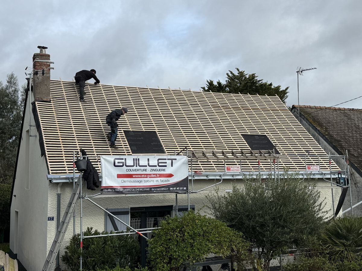 Deux couvreurs d'ETS Guillet posent le liteaunage d'une toiture, banderole de l'entreprise sur l'échafaudage