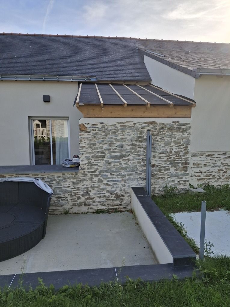 Débord de toiture en aluminium prolongeant un mur en pierre